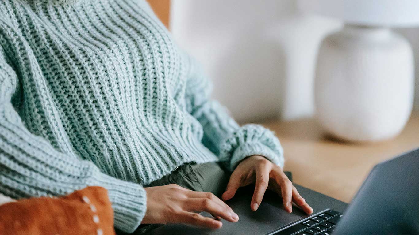 Close-up of a person in a cozy blue sweater working on a laptop — professional WordPress web design services in Colorado.